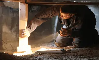 A professional inspecting wooden beams under the floor of a structure in Henderson, NV